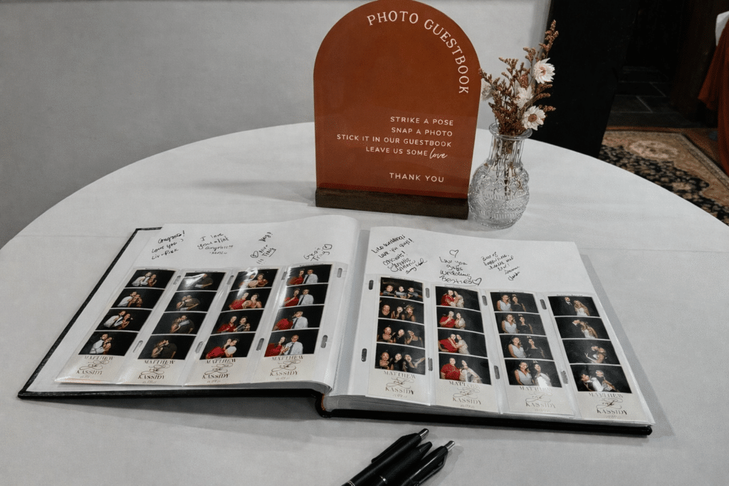 Open wedding photo booth guestbook with photo strips and handwritten messages on a decorated table.