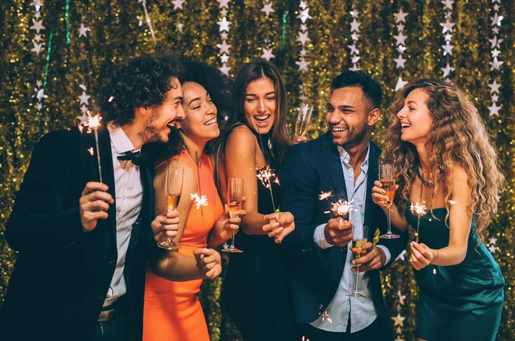 Bride and wedding guests laughing together as they pose at a wedding photo booth with sparklers